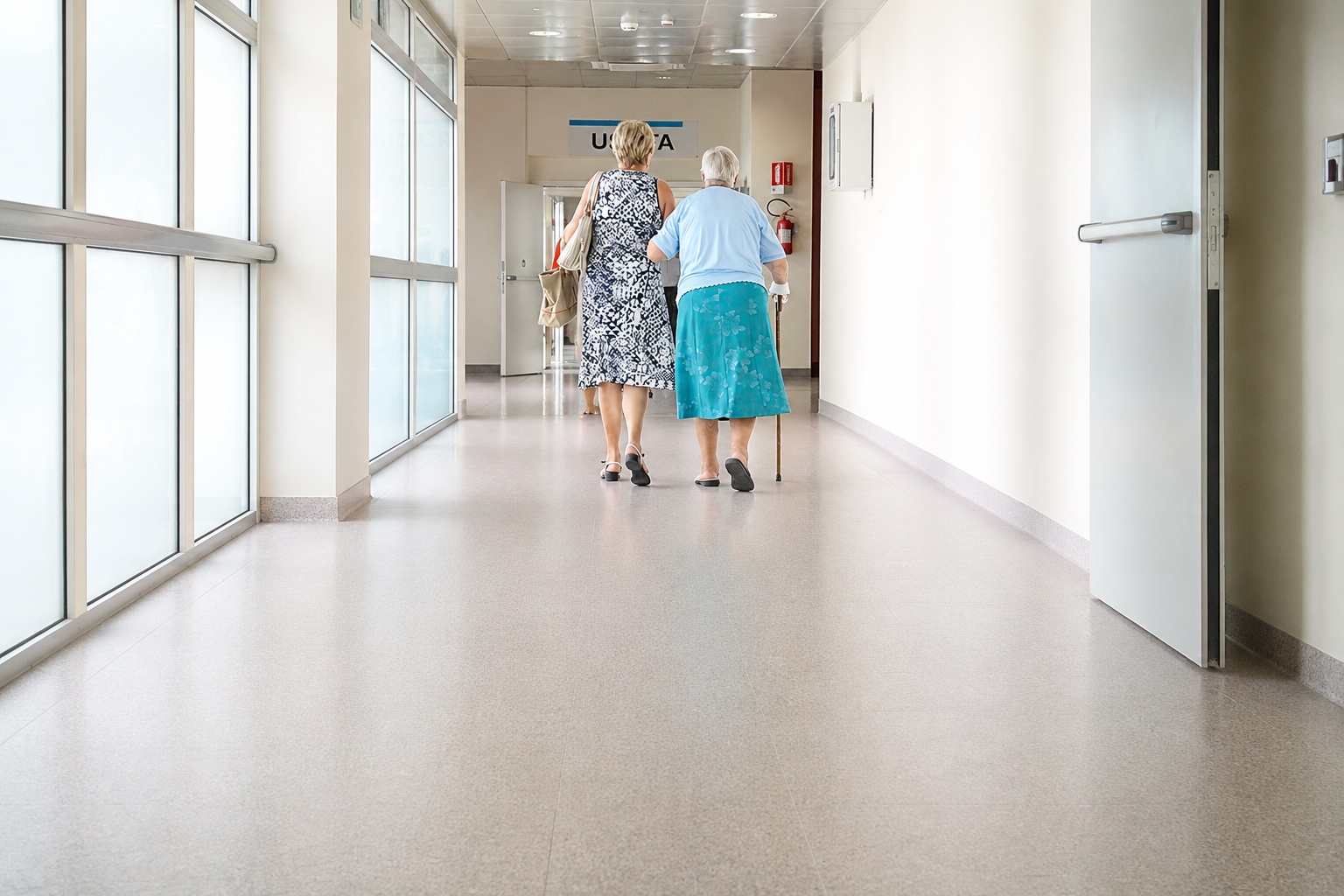 Corridoio di una casa di cura percorso da due persone, una delle quali con il bastone